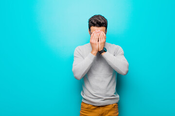 Wall Mural - young arabian man feeling sad, frustrated, nervous and depressed, covering face with both hands, crying against flat wall