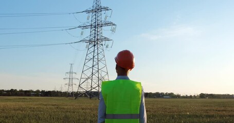 Wall Mural - a man in a protective helmet and a green signal vest looks at the power line.