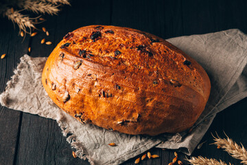 Loaf of brown bread with raisin on textile towel on black wooden background