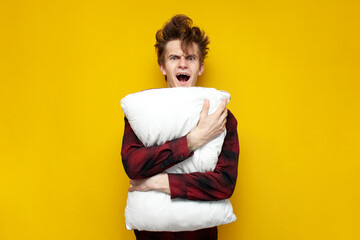 Wall Mural - sleepy tired guy holds a pillow and screams in the morning on a yellow isolated background, bad morning, man overslept