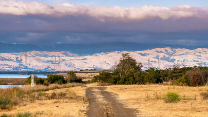 Wall Mural - Unpaved road on the shorelines of South San Francisco Bay Area; dramatic sunset clouds covering the Diablo Mountain Range visible in the background; Mountain View, California