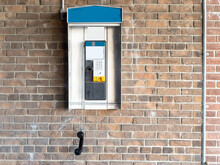 A Classic Pay Phone On A Brick Wall With The Receiver Dangling Off The Hook