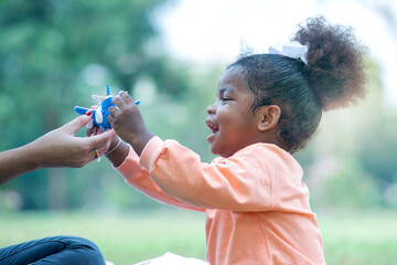 Cute dark skinned little girl enjoys with  plane toy, mother's hand sent a model of plane to her daughter in park