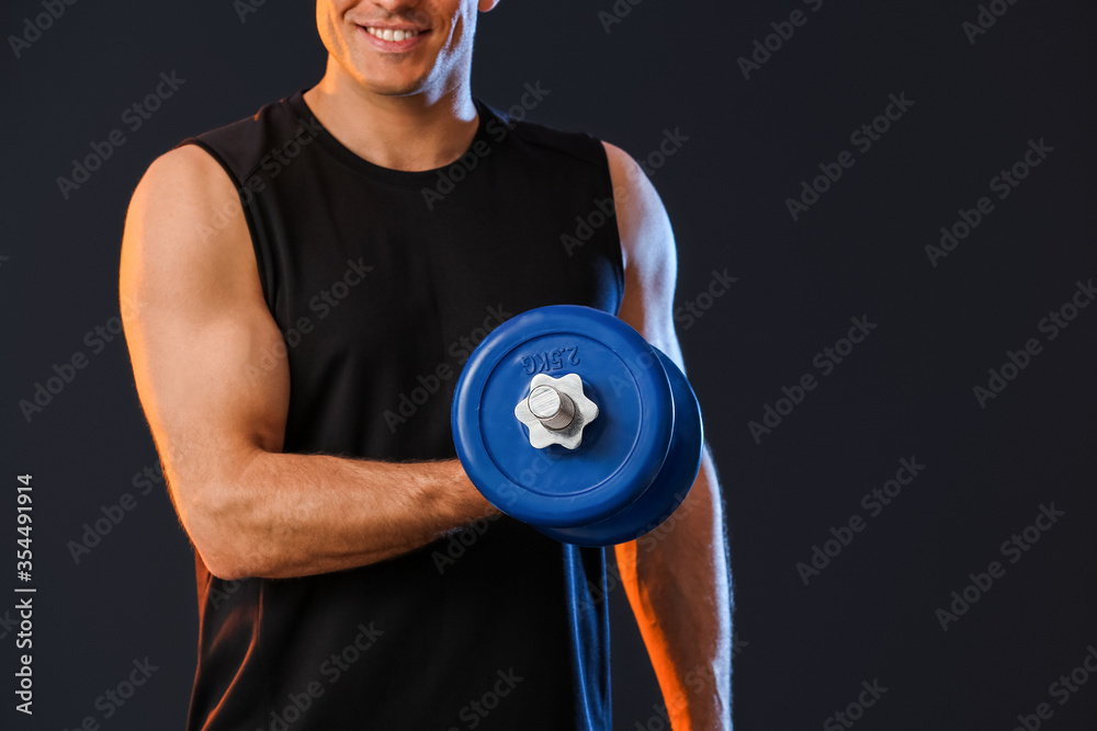 Sporty young man with dumbbell on dark background