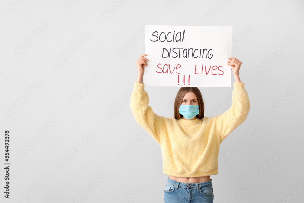 Young woman holding paper with text SOCIAL DISTANCING. SAVE LIVES on grey background. Concept of epidemic
