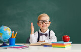 Fototapeta Panele - funny child   schoolboy    student  raises his hand up near school blackboard.