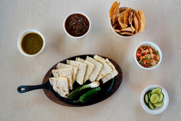 Canvas Print - High angel shot of quesadilla with chicken and sauces, chips on the table