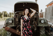 Portrait  Outdoor Atmospheric Lifestyle Photo Of Young Beautiful  Darkhaired Woman In A Black Dress In A Floral Print Against The Backdrop Of An Old Truck Car . Autumn Walking Concept