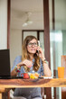 © astrosystem - Woman using laptop and cellphone at home during breakfast - freelancing concept.