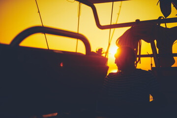 Wall Mural - Sailor steering sailing boat with a rudder in dawn / twilight time on tje open sea.