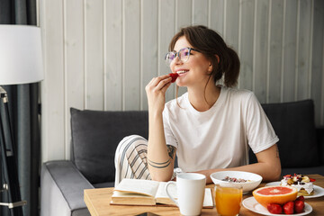 Sticker - Photo of woman reading book and eating strawberry while having breakfast