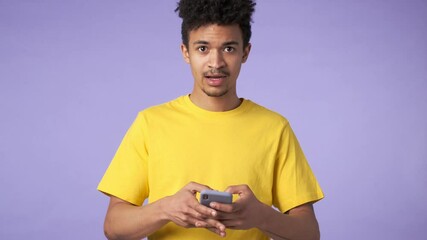 Poster - Young african emotional shocked guy isolated over purple background using mobile phone