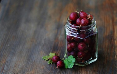 Sticker - Red gooseberry in a glass jar on an old wooden background. Canning of berries. Planned to make jam from gooseberry. Soft focus. Place for text.copy space 