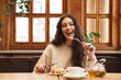 © Drobot Dean - Image of woman smiling and eating pancakes while sitting in cozy cafe