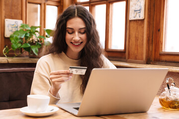 Canvas Print - Image of woman using laptop and holding credit card while drinking tea