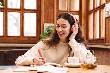 Canvas Print - Image of joyful student woman using headphones while doing homework