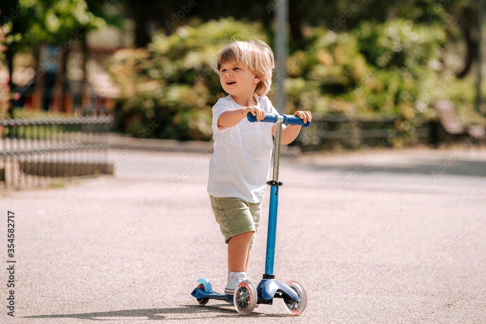 Boy learn to ride scooter in a park on sunny summer day. Preschooler ...