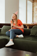 © LIGHTFIELD STUDIOS - selective focus of happy woman in party cap sitting on sofa and holding glass of red wine