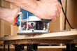 © stockphoto-graf - closeup of carpenter with hand wood router machine at work. closeup of routing bevel into plank of pine woodworking construction tool concept furniture making diy background
