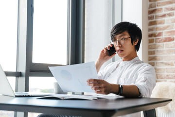 Sticker - Image of asian man using cellphone and holding paper documents in office