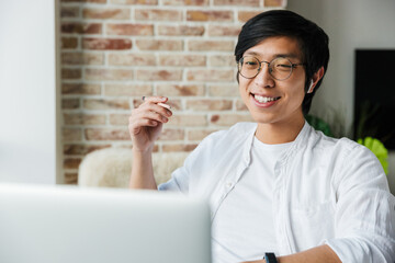 Sticker - Image of young asian man wearing earphones using laptop in office