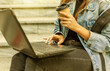 © splitov27 - Happy modern woman student in denim jacket and backpack sitting on the stairs and uses laptop outdoor. Drinks coffee. Distance learning. Modern youth concept.