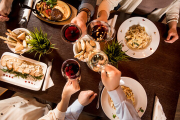 Four hands with red wine toasting over served table with food