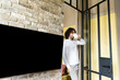 © LIGHTFIELD STUDIOS - young man in pajamas drinking coffee while standing near blank lcd screen hanging on brick wall