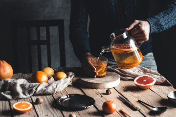 A man pours citrus tea on a wooden table. Healthy drink, vintage style. Vegan, eco products.