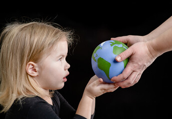 Wall Mural - Parent gives the planet into the hands of a baby girl. Isolated on dark background