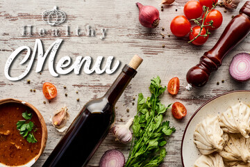 Wall Mural - top view of delicious khinkali near bottle of wine, kharcho, vegetables and spices on wooden table, healthy menu illustration