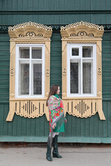 Russian girl in Pavlovo Posad shawl. Wooden traditional rural house with ornamental carved windows, frames in Ivanovo city, Russia. Russian folk style in architecture, architectural fashion. Landmark