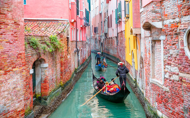 Wall Mural - Venetian gondolier punting gondola through green canal waters of Venice Italy