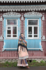 Russian girl in Pavlovo Posad shawl. Wooden traditional rural house with ornamental carved windows, frames in Ivanovo city, Russia. Russian folk style in architecture, architectural fashion. Landmark