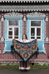 Russian girl in Pavlovo Posad shawl. Wooden traditional rural house with ornamental carved windows, frames in Ivanovo city, Russia. Russian folk style in architecture, architectural fashion. Landmark