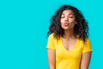 Wall Mural - Portrait of beautiful smiling dark skinned girl wearing bright colored yellow t-shirt isolated over blue background