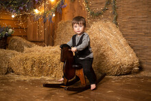Boy Riding Wooden Traditional Rocking Horse Toy In Farm Background With Straw Sheaves.