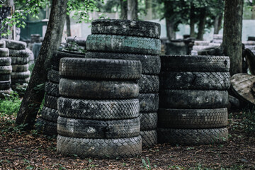 Paintball shooting range. Paintball territory in the forest. Iron barrels in the foreground with multi-colored blots and smudges from shots from the paintball weapon. Old tires from a car and trees. 