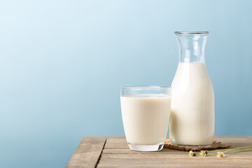 Wall Mural - A glass and bottle of milk on wooden table with light blue background.