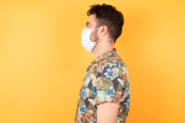 Young caucasian man wearing hawaiian shirt and medical mask looking to side, relax profile pose with natural face with confident smile.