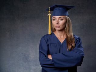 Serious young female graduate arms crossed wearing blue cap and gown