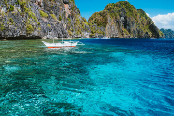 banca boat moored und crystal clear ocean water near matinloc island, highlights of hopping trip tou