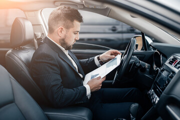 Handsome caucasian businessman driver inside in vehicle  with coffee and gadget and check mail and talking with partners