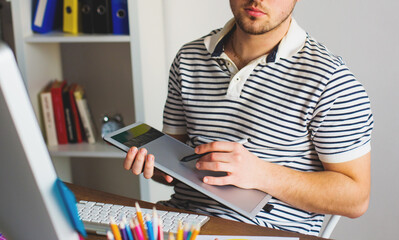 Wall Mural - Young Handsome Graphic designer using graphic tablet to do his work at desk