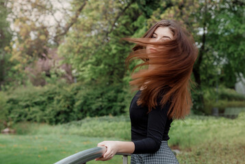 Beautiful girl walks in a green park. Young woman with long black hair, wearing a black jacket and short skirt. A walk in the garden of the Library of the University of Warsaw. Hair movement.