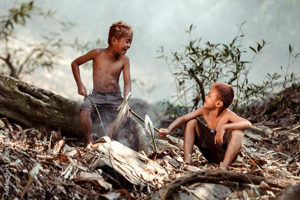 Two boys Are using fish to cook on the side of a stream near their home ...