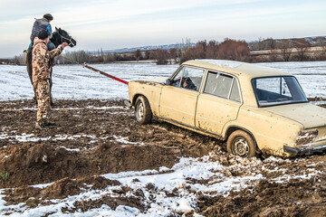A horse pulls out a car stuck in a field in the mud on a sunny day.