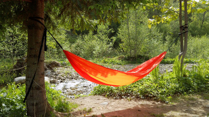 orange hammock hanging tied to two trees at the nature.