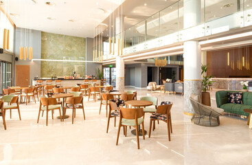 Light wooden and marble tile floor interior of modern cafe with double ceiling height. Lobby bar in luxury design hotel hall with second split level