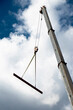 Construction crane with a hook and a metal profile hanging on ropes, low angle view with cloudy sunny blue sky